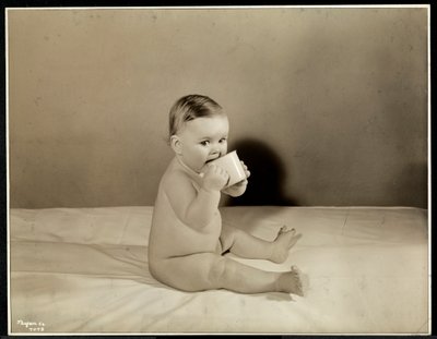 Un bebé sentado en la cama bebiendo de una taza en el Centro de Maternidad en la Calle 70 East River, Nueva York, 1935 (impresión de gelatina de plata) de Byron Company